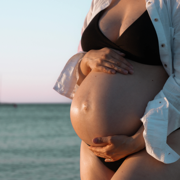 Expecting mother posing gracefully by the ocean, celebrating her pregnancy journey with stunning beach scenery.