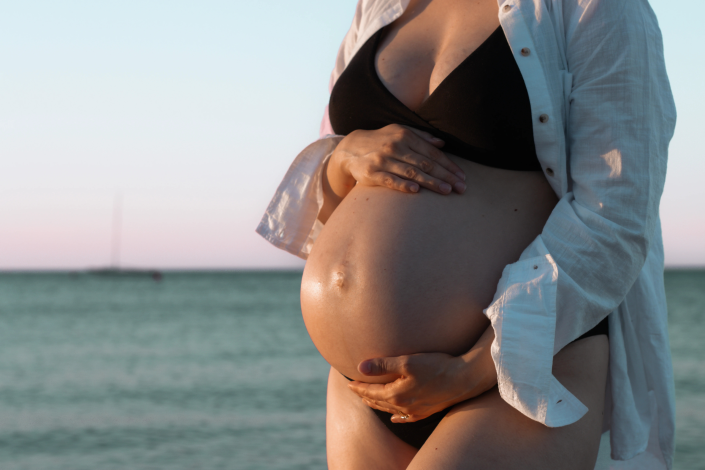 Expecting mother posing gracefully by the ocean, celebrating her pregnancy journey with stunning beach scenery.