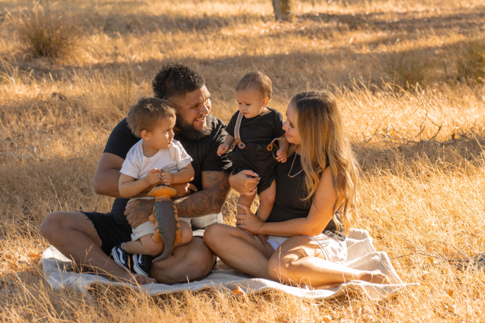 Family sharing snacks on blanket, toddler feeding parent a strawberry, genuine laughter captured in candid moment