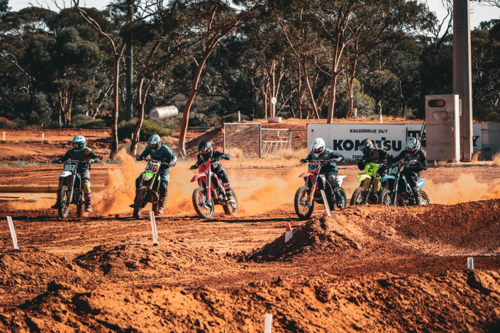 A group of motocross riders racing side by side on a dirt track, with spectators cheering in the background."