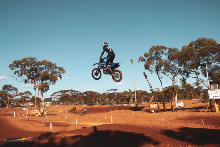 A motocross rider soaring through the air during a jump, with dirt flying behind them at the dirt bike event.