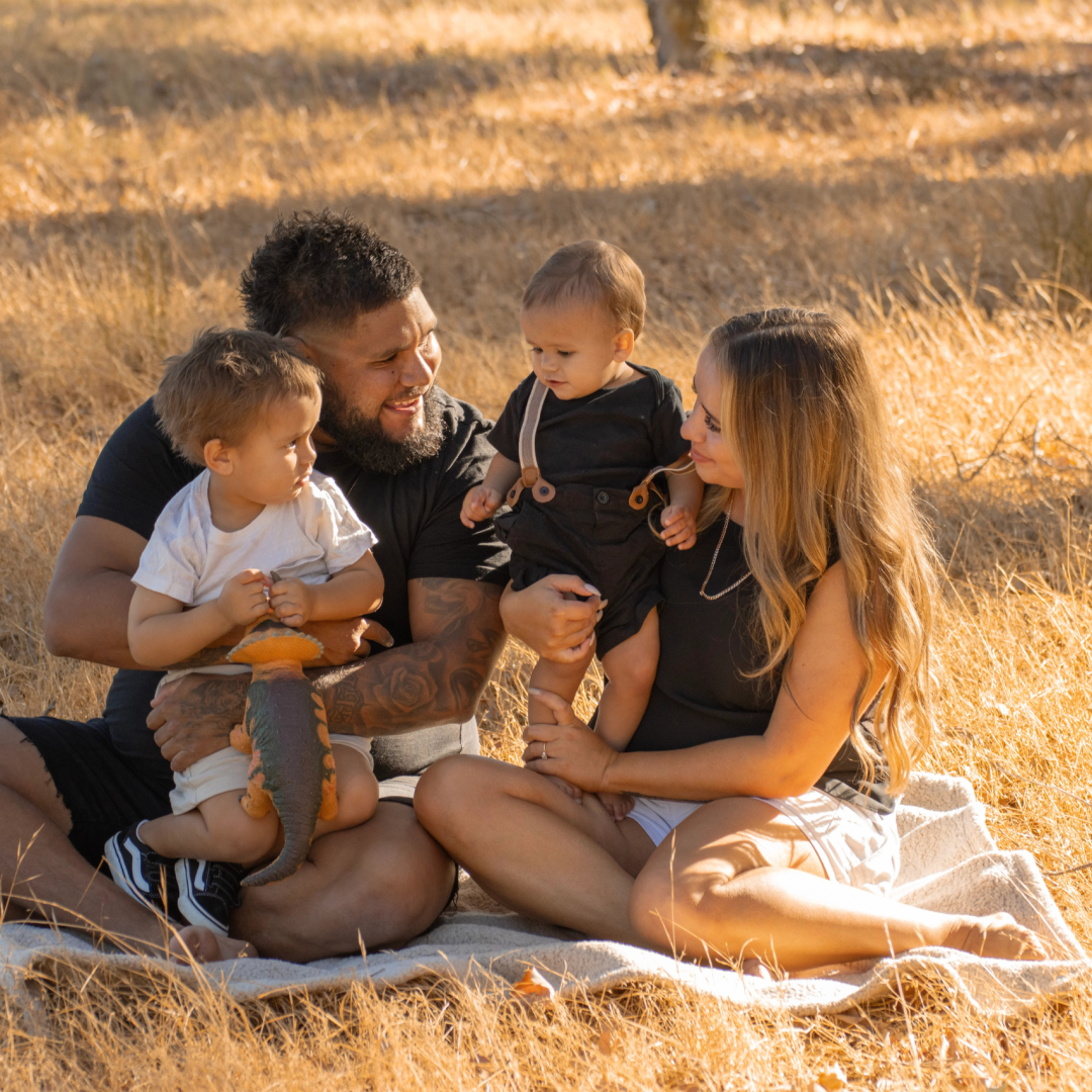 Family sharing snacks on blanket, toddler feeding parent a strawberry, genuine laughter captured in candid moment